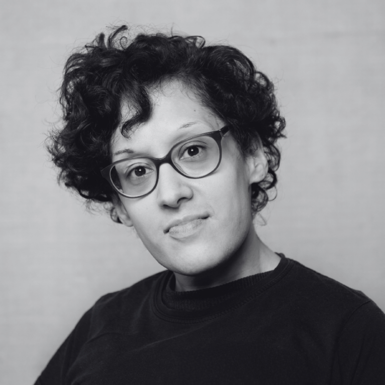 Black and white headshot of a woman with short curly hair and glasses.