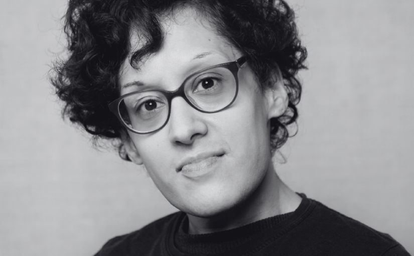 Black and white headshot of a woman with short curly hair and glasses.