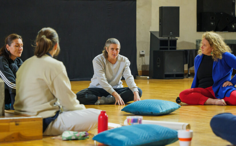A small group of women sitting in a circle on cushions on the floor while attending a class.