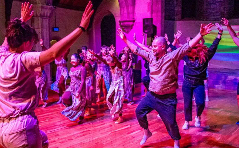 Rose-tinted image of a group of people dancing and jumping up with their arms in the air.