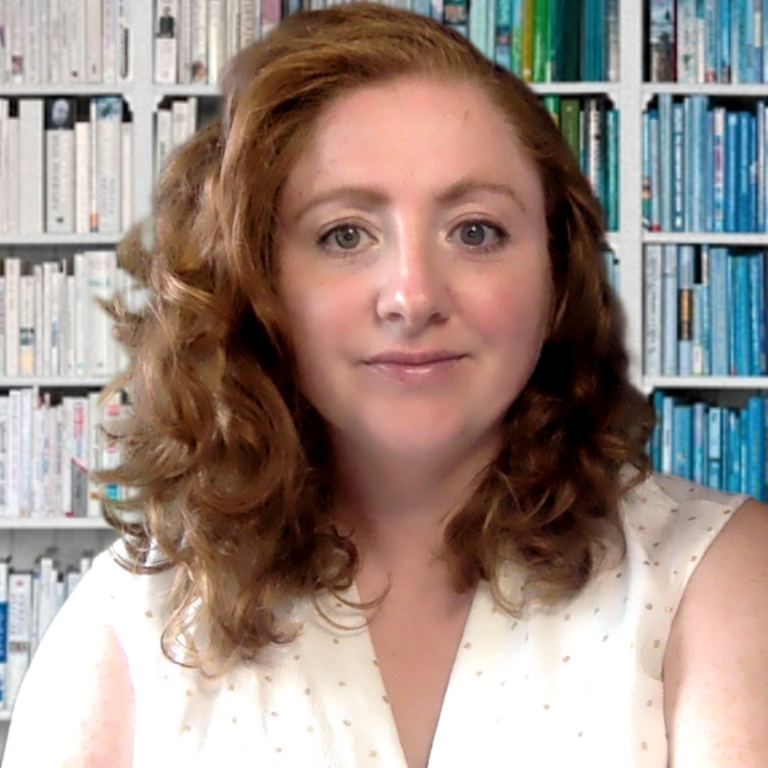 Headshot of a woman with red curly hair in a white sleeveless shirt against a background of bookshelves.