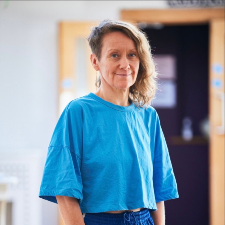 Image of a woman with wavy blonde hair wearing a bright blue t-shirt against a light background.