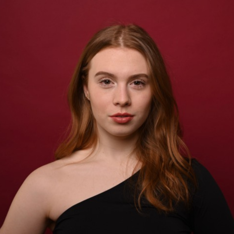 Headshot of a young woman with long red hair against a burgundy background.