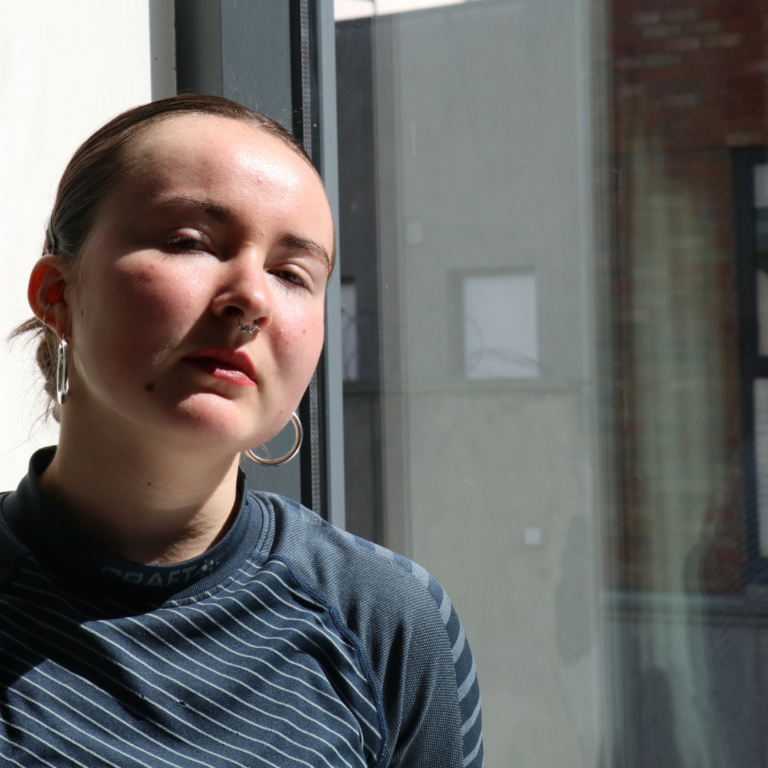 Headshot of a young woman with dark hair pulled back in front of a window.