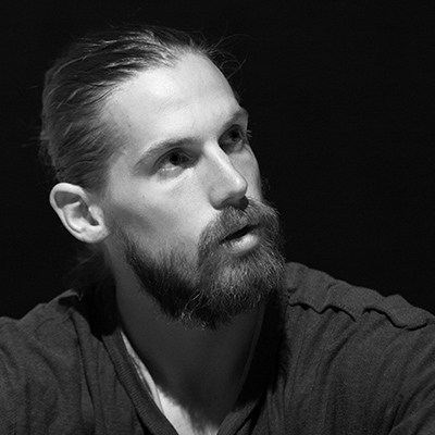 Black and white headshot of a young band with a beard and moustache looking to the right.