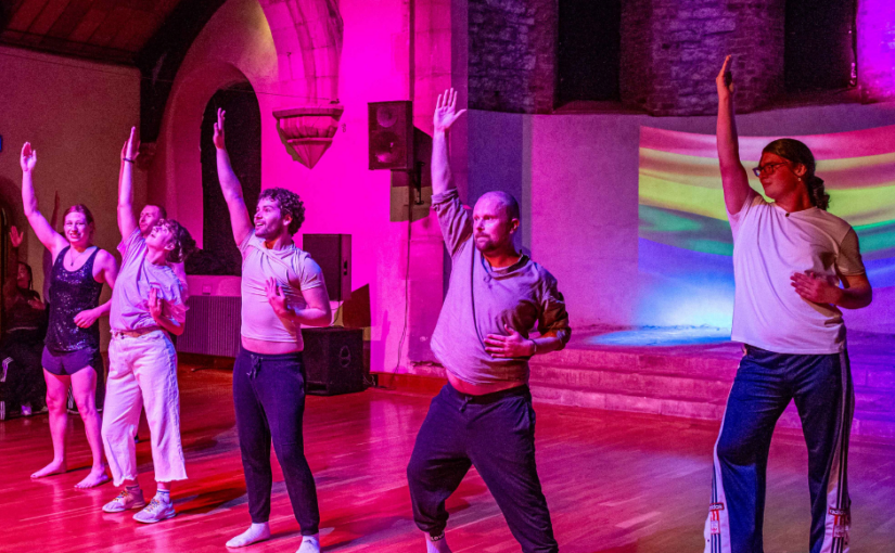 Rose-tinted image of a group of people dancing raising their right hands in the air.