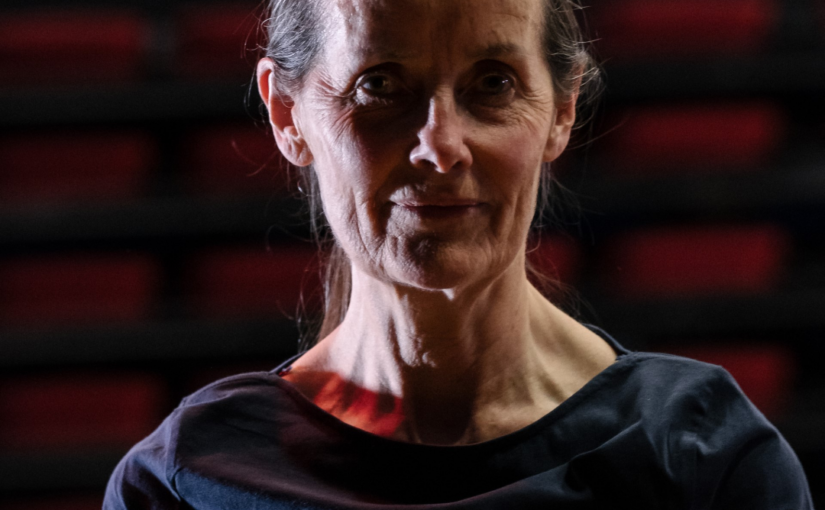 Headshot of a woman wearing a dark blue shirt against a burgundy background.