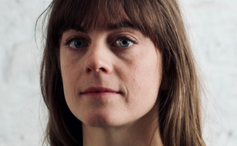 Headshot of a woman with long, light brown hair against a light grey background.