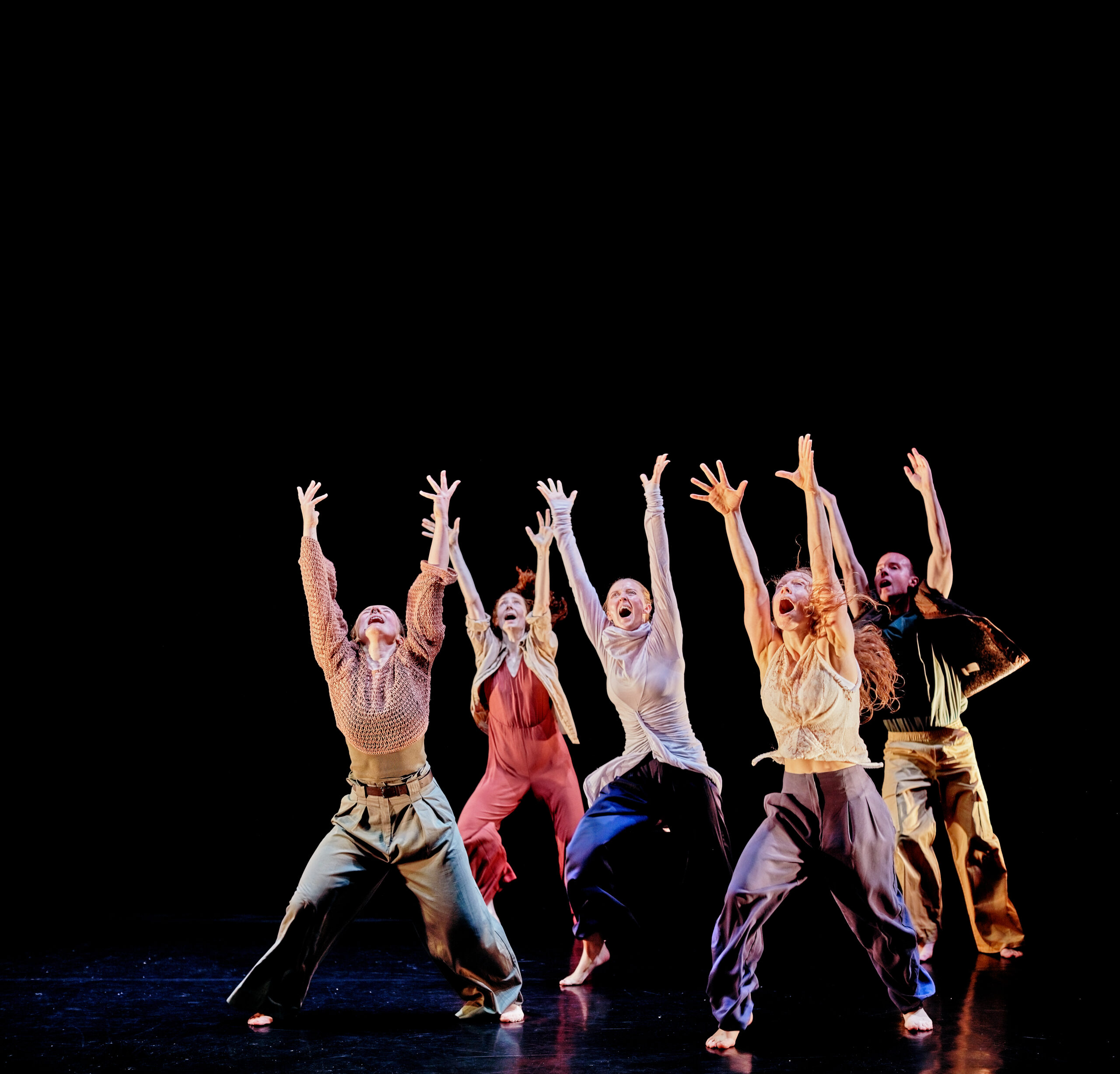 Image of five dancers lifting their arms in the air against a dark background.