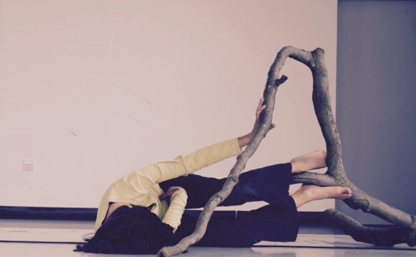 Image of a dancer lying on the floor with her feet on a tree branch.