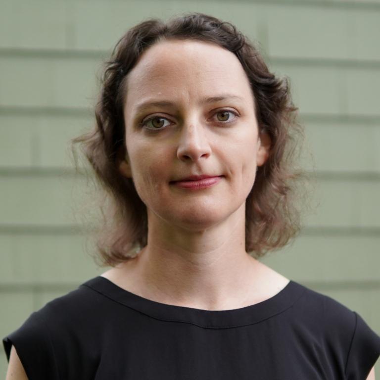 Headshot of a woman with short hair against a green brick background.