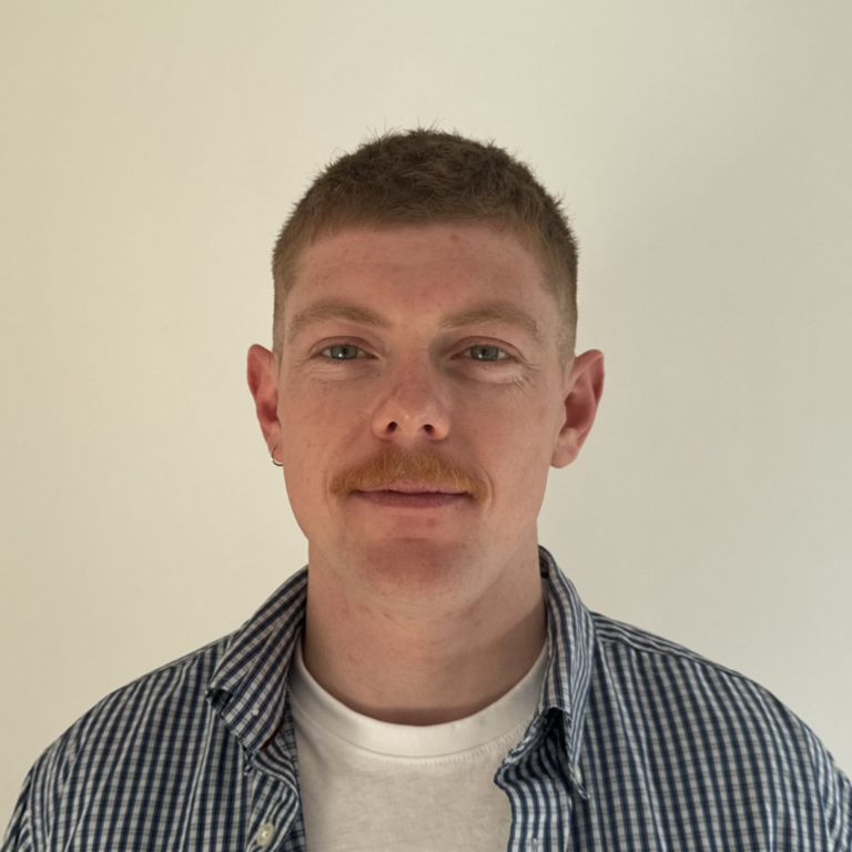 Headshot of a man with a chequered shirt against a clear background.