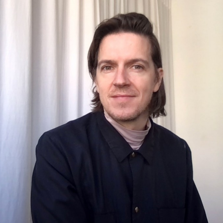 Headshot of a man wearing a dark jacket against a set of light curtains.