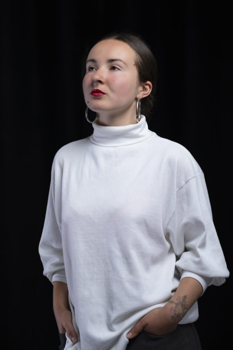 Headshot of a woman wearing a white jumper against a black background.