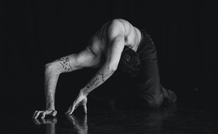 Image of a bare-chested dancer making a sculptural form with his arms.