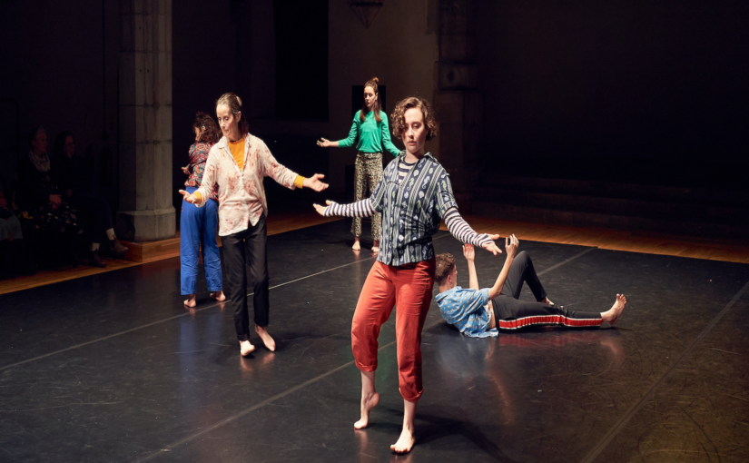 Image of five dancers in a performance space with their arms extended, holding different poses.