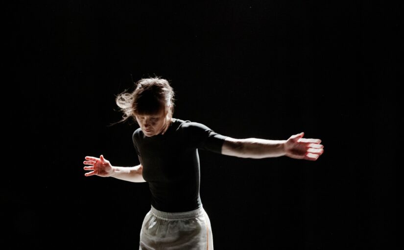 Photo of a dancer with her arms stretched to both sides against a black background.
