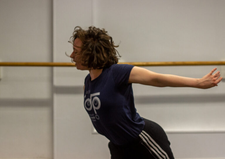 Photo of a dancer moving in a dance studio with ballet bars in the background.